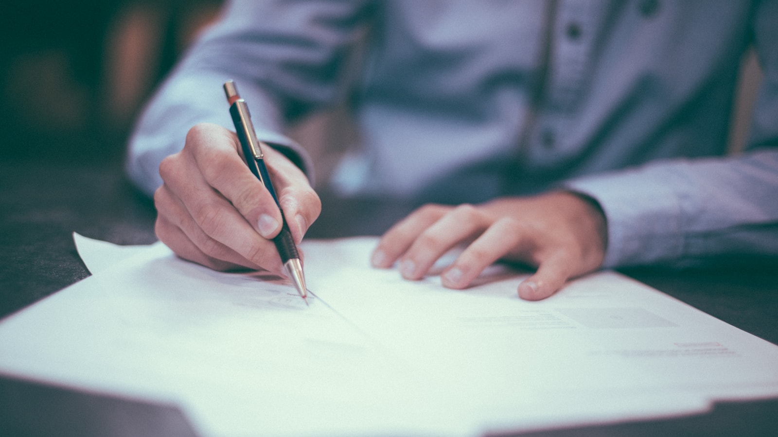 Hands writing on documents at a desk during careful review